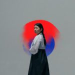 Woman in traditional Korean dress looking back against grey backdrop and red/blue circle